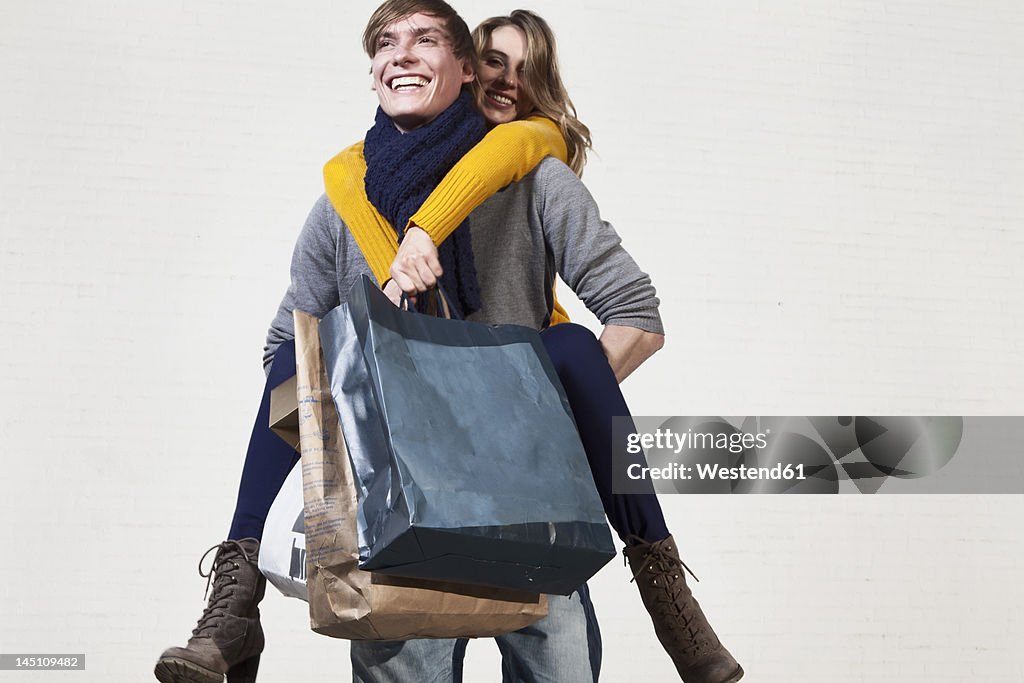 Germany, Bavaria, Munich, Young man carrying woman on his back while she holds shopping bags