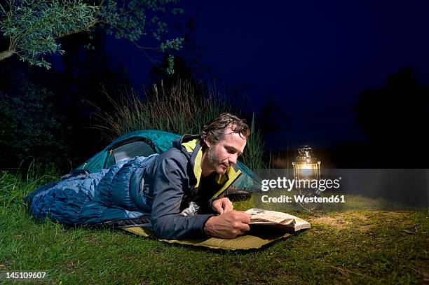 germany, bavaria, ammersee, man reading book near lakeshore while camping at night - saco de dormir fotografías e imágenes de stock