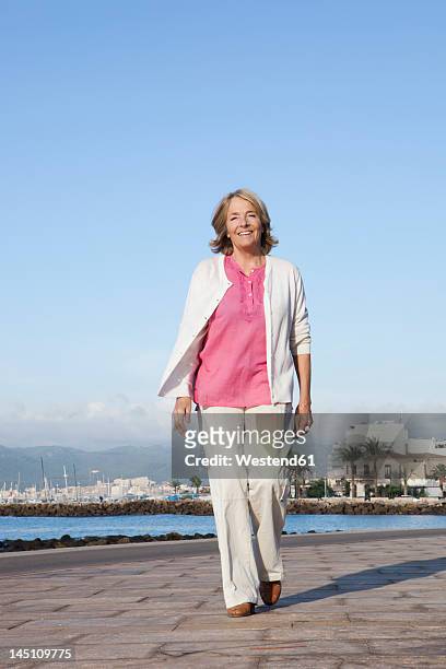 spain, mallorca, senior woman walking along sea shore, smiling - só uma mulher idosa imagens e fotografias de stock