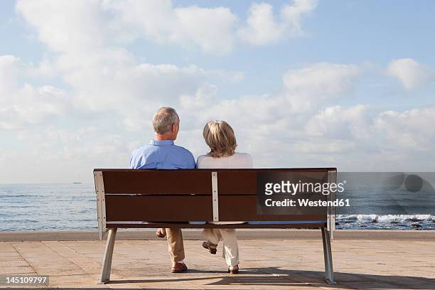 spain, mallorca, senior couple sitting on bench at sea shore - bench foto e immagini stock