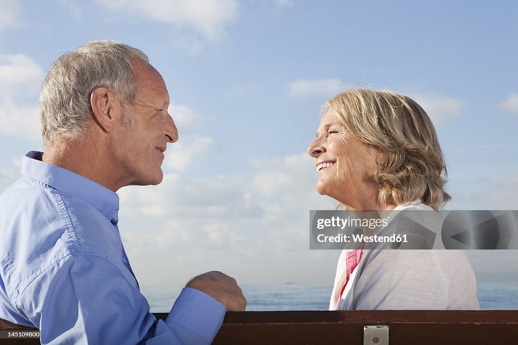 Spain, Mallorca, Senior couple sitting on bench at sea shore, smiling