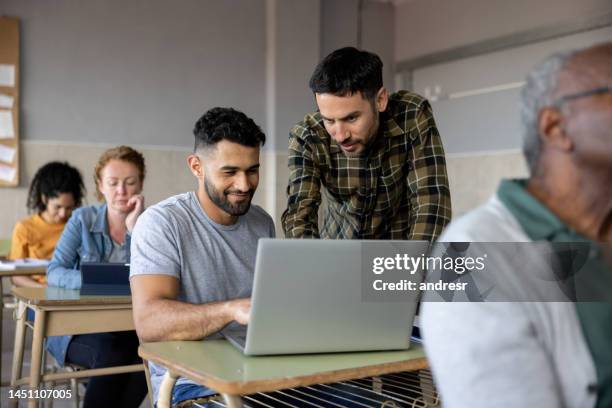 teacher helping a student in class while using a laptop computer - avondschool stockfoto's en -beelden