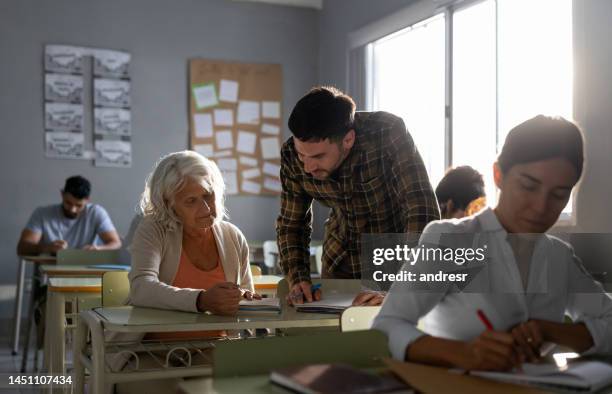 teacher helping a senior woman taking his class - avondschool stockfoto's en -beelden