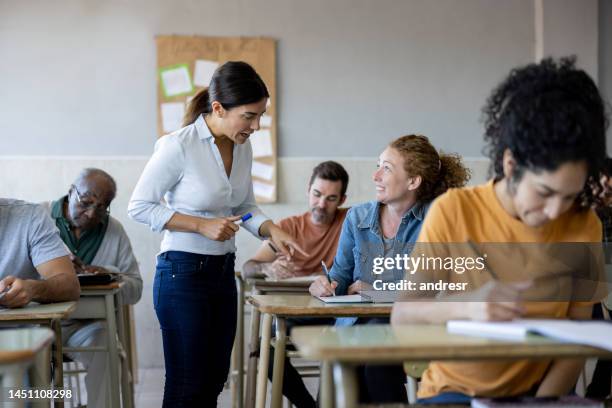 happy teacher helping a student in class - avondschool stockfoto's en -beelden
