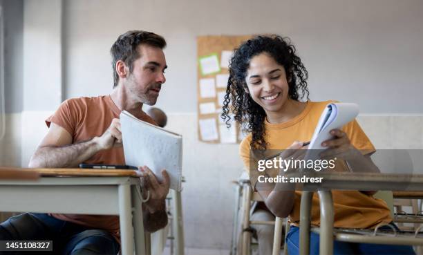 two students sharing notes in class and looking very happy - avondschool stockfoto's en -beelden