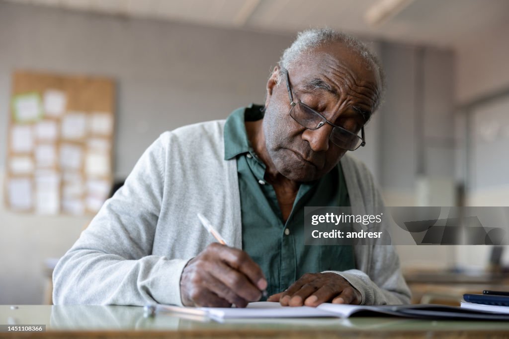 Senior man studying in college and writing on his notebook in the classroom