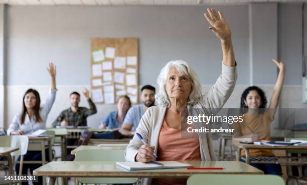 adult student raising her hand to ask a question in class - avondschool stockfoto's en -beelden