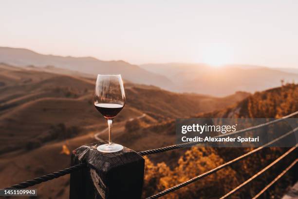 glass of red wine at sunset against hills and mountains - vino tinto fotografías e imágenes de stock