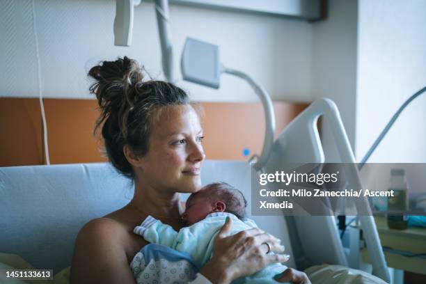 mother holds newborn baby in hospital bed - family photo in the delivery room stock-fotos und bilder