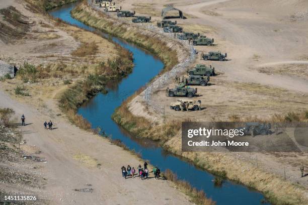 As seen from an aerial view, Migrants walk along the Mexican side of the Rio Grande as Texas National Guard and state police stand guard across the...