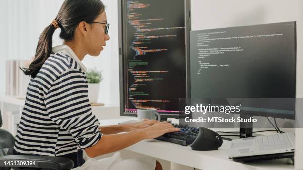 las jóvenes desarrolladoras de software asiáticas que usan la computadora para escribir código sentadas en el escritorio con múltiples pantallas trabajan de forma remota en casa. - aprendizaje automático fotografías e imágenes de stock