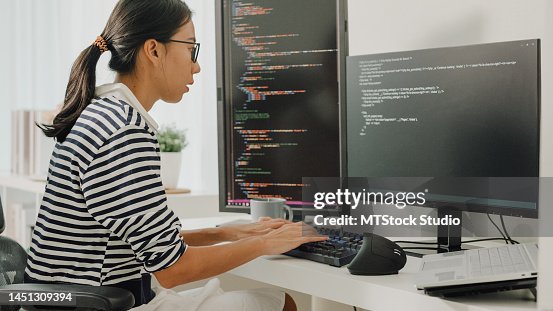 Young Asian woman software developers using computer to write code sitting at desk with multiple screens work remotely at home. Young Asian woman software developers using computer to write code sitting at desk with multiple screens work remotely at home.
