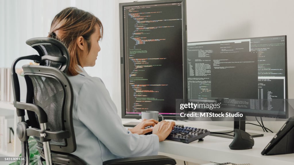 Les jeunes développeuses asiatiques de logiciels utilisant un ordinateur pour écrire du code assises à un bureau avec plusieurs écrans travaillent à distance à la maison.