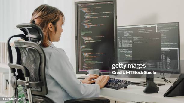 young asian woman software developers using computer to write code sitting at desk with multiple screens work remotely at home. - vetenskapskvinna bildbanksfoton och bilder