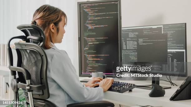 young asian woman software developers using computer to write code sitting at desk with multiple screens work remotely at home. - programmer 個照片及圖片檔