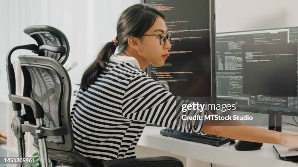 young asian woman software developers using computer to write code sitting at desk with multiple screens work remotely at home. - datawetenschapper stockfoto's en -beelden