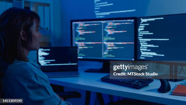 young asian woman software developers using computer to write code sitting at desk with multiple screens work remotely in home at night. - datawetenschapper stockfoto's en -beelden