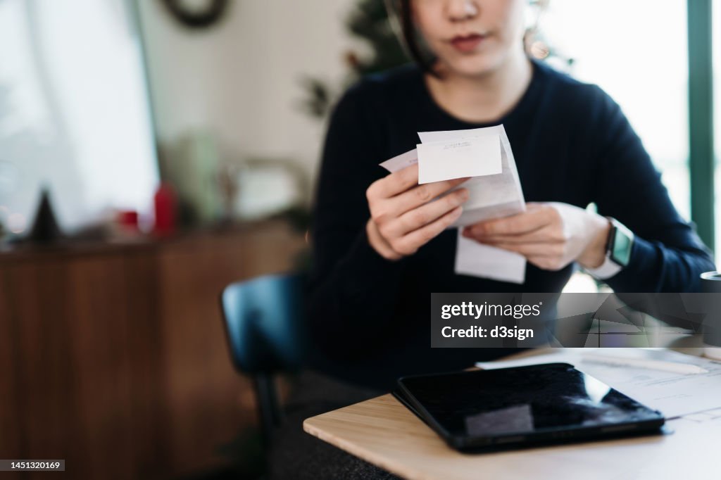 Young Asian woman managing personal banking and finance. Planning budget and calculating expenses with digital tablet while going through various expense receipts at home after shopping. Home finances. Home budgeting. Banking and finance concept