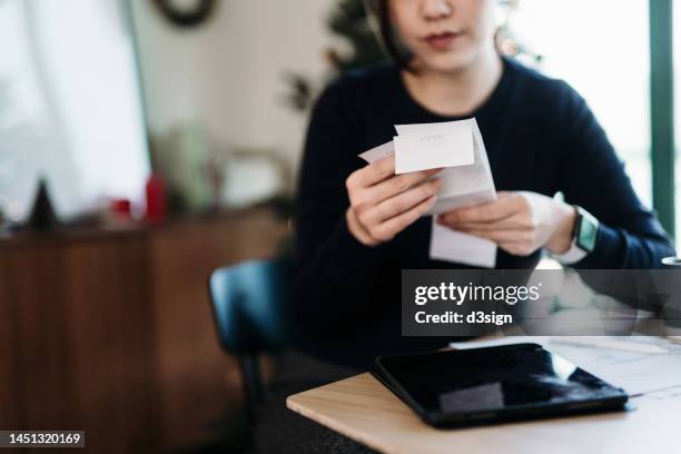 young asian woman managing personal banking and finance. planning budget and calculating expenses with digital tablet while going through various expense receipts at home after shopping. home finances. home budgeting. banking and finance concept - orçamento imagens e fotografias de stock