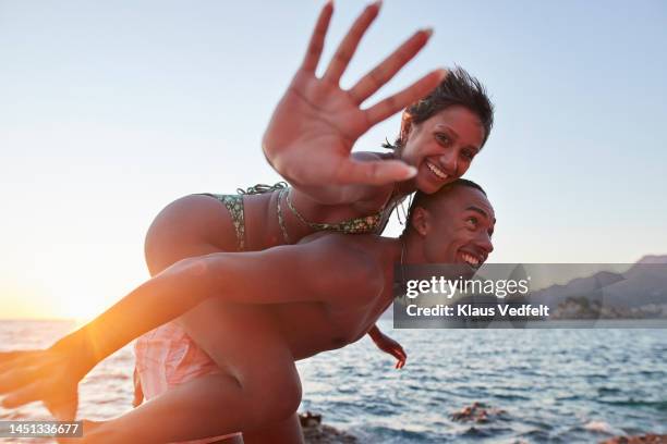 happy woman enjoying piggyback ride on boyfriend - friends waving stock pictures, royalty-free photos & images