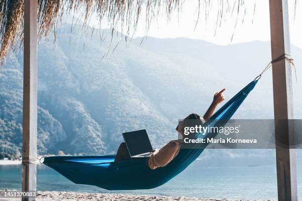 tourist on summer vacation combining work and leisure. woman using laptop in hammock on beach. - working life balance stock pictures, royalty-free photos & images