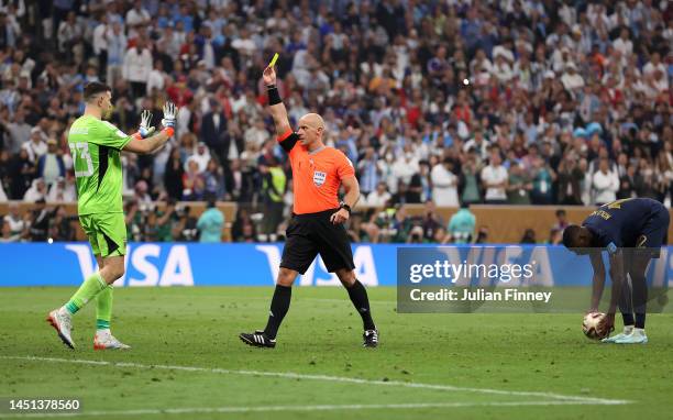 Emiliano Martinez of Argentina receives a yellow card from referee Szymon Marciniak after he attempted to disturb Randal Kolo Muani of France in the...