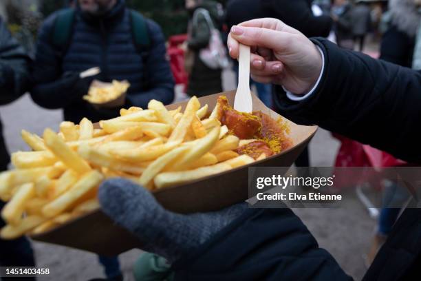 over the shoulder view of woman eating chips and curry sausage from a paper tray at a german christmas market. - currywurst stock pictures, royalty-free photos & images