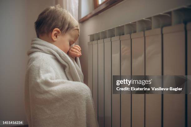 a child freezing in an apartment warming himself in a blanket by the battery - daily life in zagreb stock pictures, royalty-free photos & images