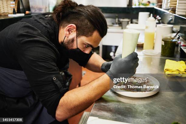 medium shot of chef garnishing plate of fresh tuna carpaccio - paire de gants noirs photos et images de collection