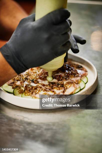 close up shot of chef garnishing plate of fresh tuna carpaccio - luva preta imagens e fotografias de stock