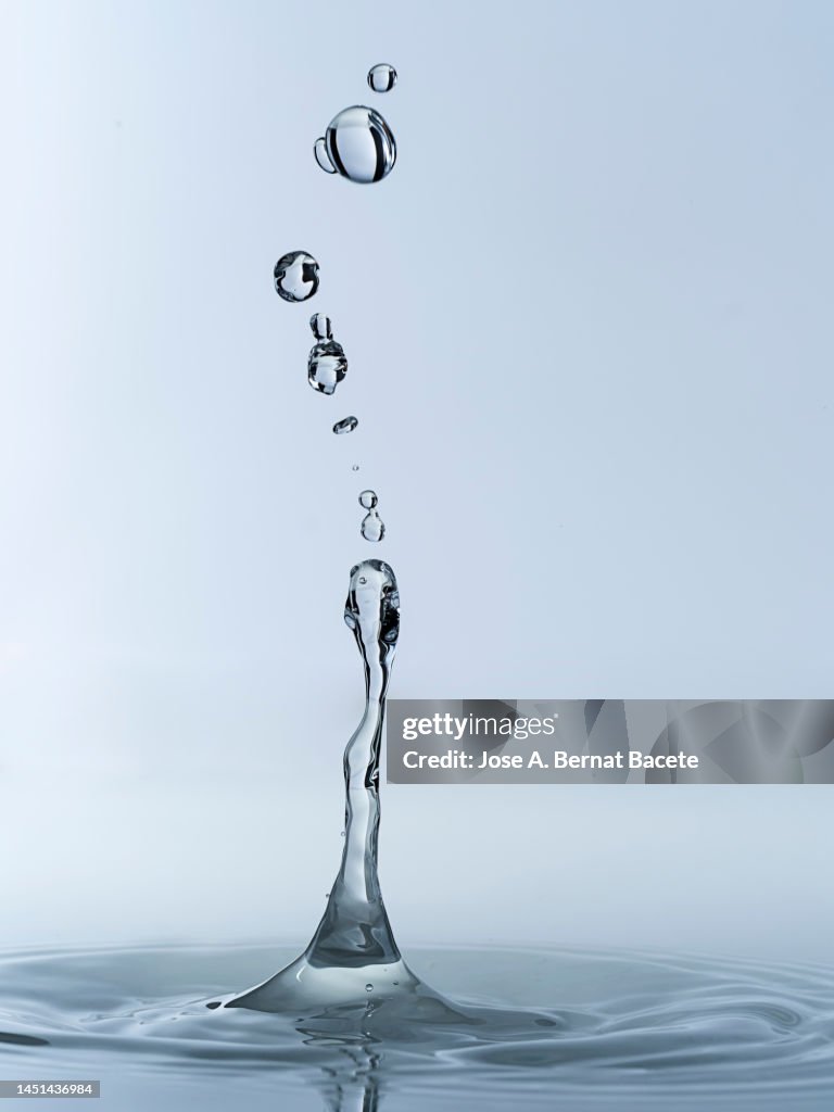 Group of water droplets fall and bounce on a water surface.