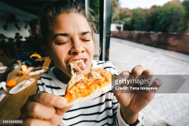 young woman is eating cheese pizza with pleasure - pizza fotografías e imágenes de stock