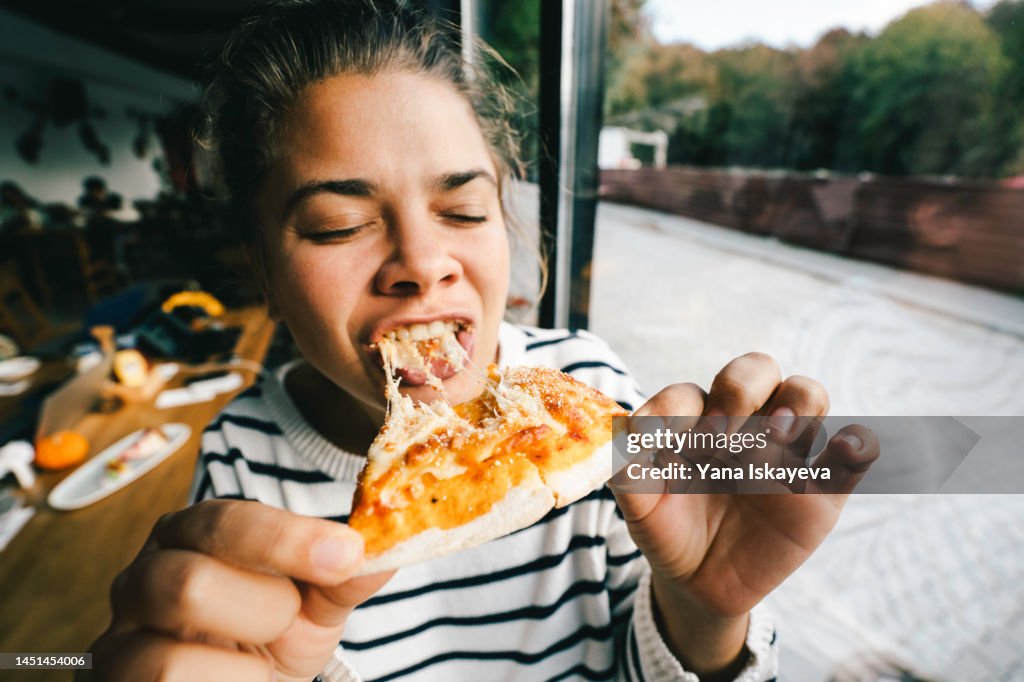 Young woman is eating cheese pizza with pleasure