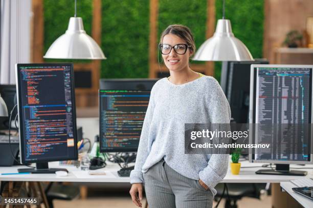 portrait of young smiling female programmer, standing in front of her desk with computers in an it office - female programmer stock pictures, royalty-free photos & images