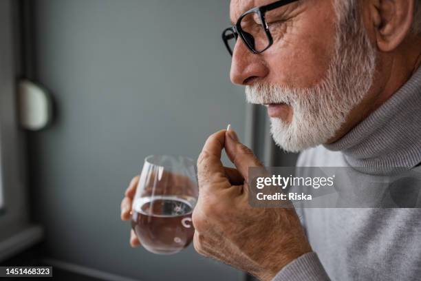 senior man taking a medical pill - taking medication stockfoto's en -beelden