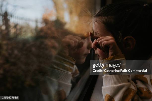 a little girl presses her nose and finger against a train window - peep window stock-fotos und bilder