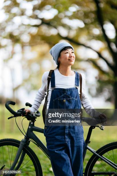 bella donna asiatica che si gode una giornata nel parco con la bicicletta - salopette foto e immagini stock