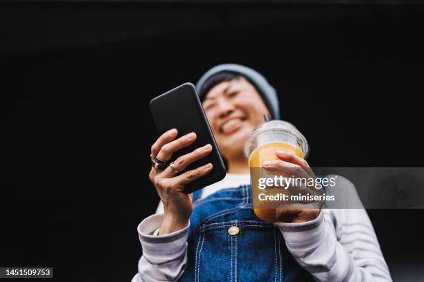 anonymous woman holding a phone and a plastic cup with orange juice - zoom in stock pictures, royalty-free photos & images