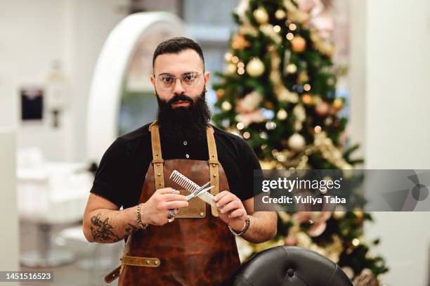 ritratto di un uomo barbuto sicuro di sé che tiene in mano strumenti di lavoro e guarda la macchina fotografica. - barbiere foto e immagini stock