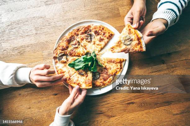 two friends having a pizza on a wooden table - pizza fotografías e imágenes de stock