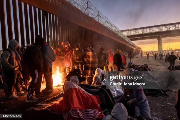 Immigrants keep warm by a fire at dawn after spending the night outside next to the U.S.-Mexico border fence on December 22, 2022 in El Paso, Texas....