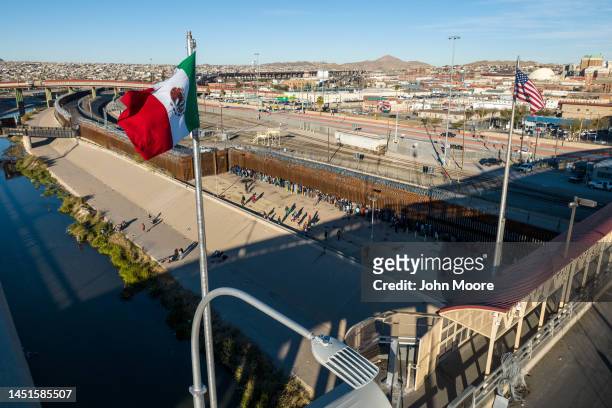 An aerial view of the Mexican and American flags fly over an international bridge as immigrants line up next to the U.S.-Mexico border fence to seek...