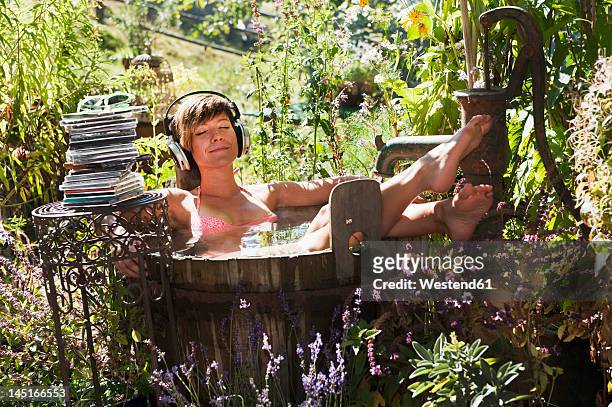 austria, salzburg, flachau, young woman sitting in tun with water and hearing music, smiling - kessel stock-fotos und bilder