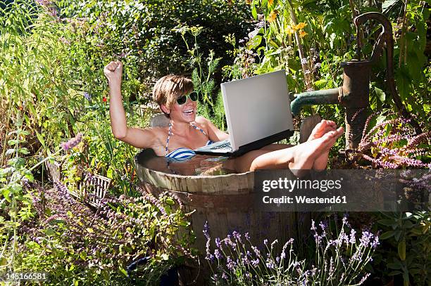 austria, salzburg, flachau, young woman sitting in tun with water and using laptop - water garden fotografías e imágenes de stock