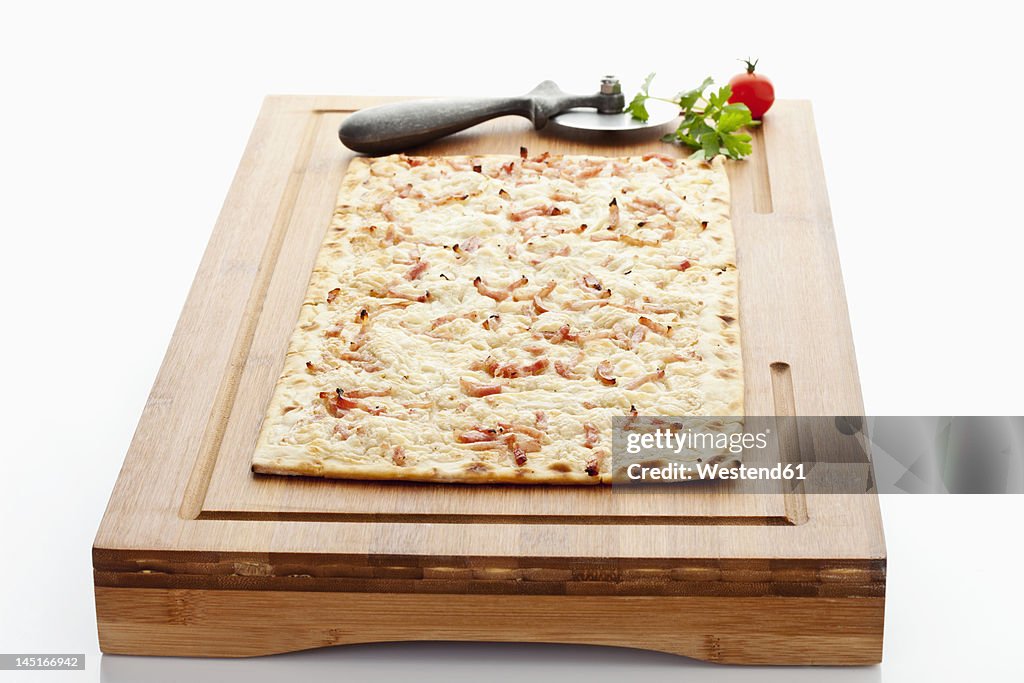 Tarte flambee with pizza cutter on wood board