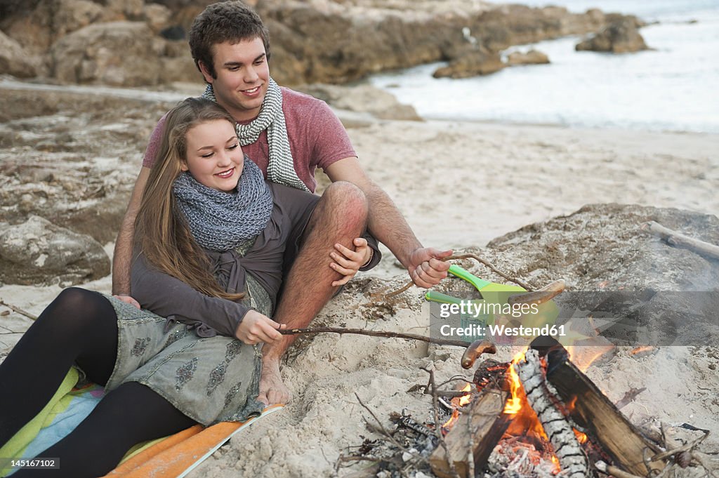 Spain, Mallorca, Couple preparing sausages on beach, smiling