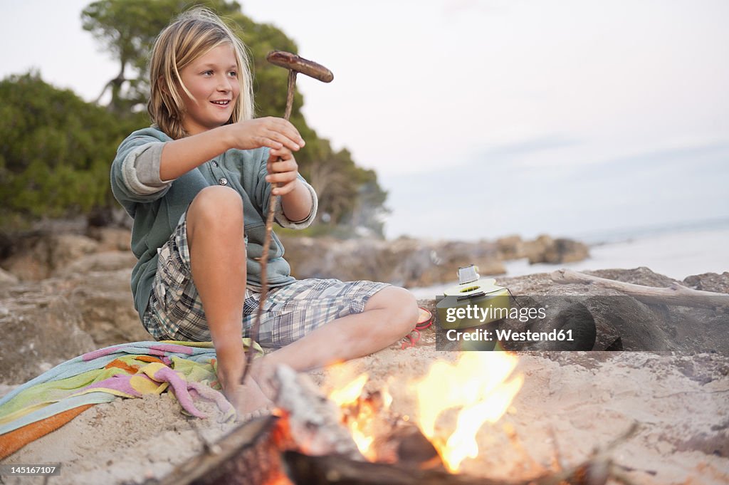 Spain, Mallorca, Boy barbecueing sausage on beach, smiling, portrait