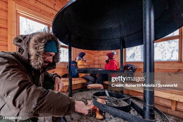 tourists warming up with fireplace inside a chalet - hut interior stock pictures, royalty-free photos & images