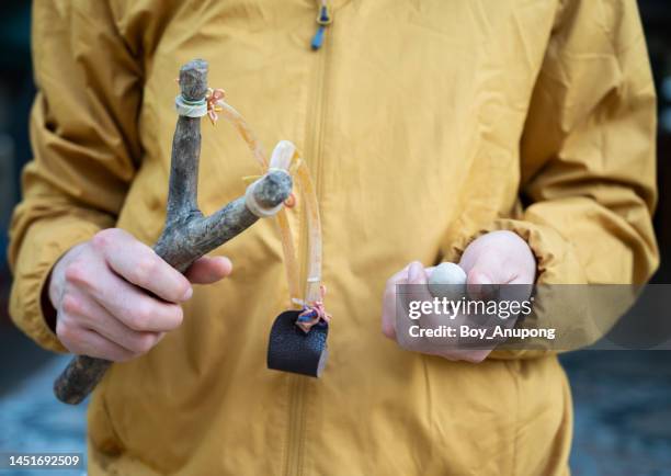 cropped shot of woman holding a wood slingshot with clay bullet in her hands.  a slingshot works like a small catapult, with rubber strips holding a stone or other projectile sits. - catapult stock pictures, royalty-free photos & images