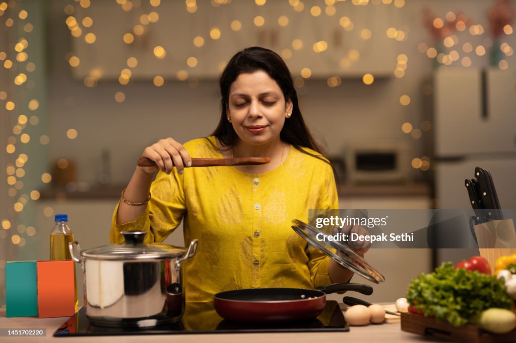 Portrait of Indian woman enjoying while cooking meal in the kitchen. stock photo